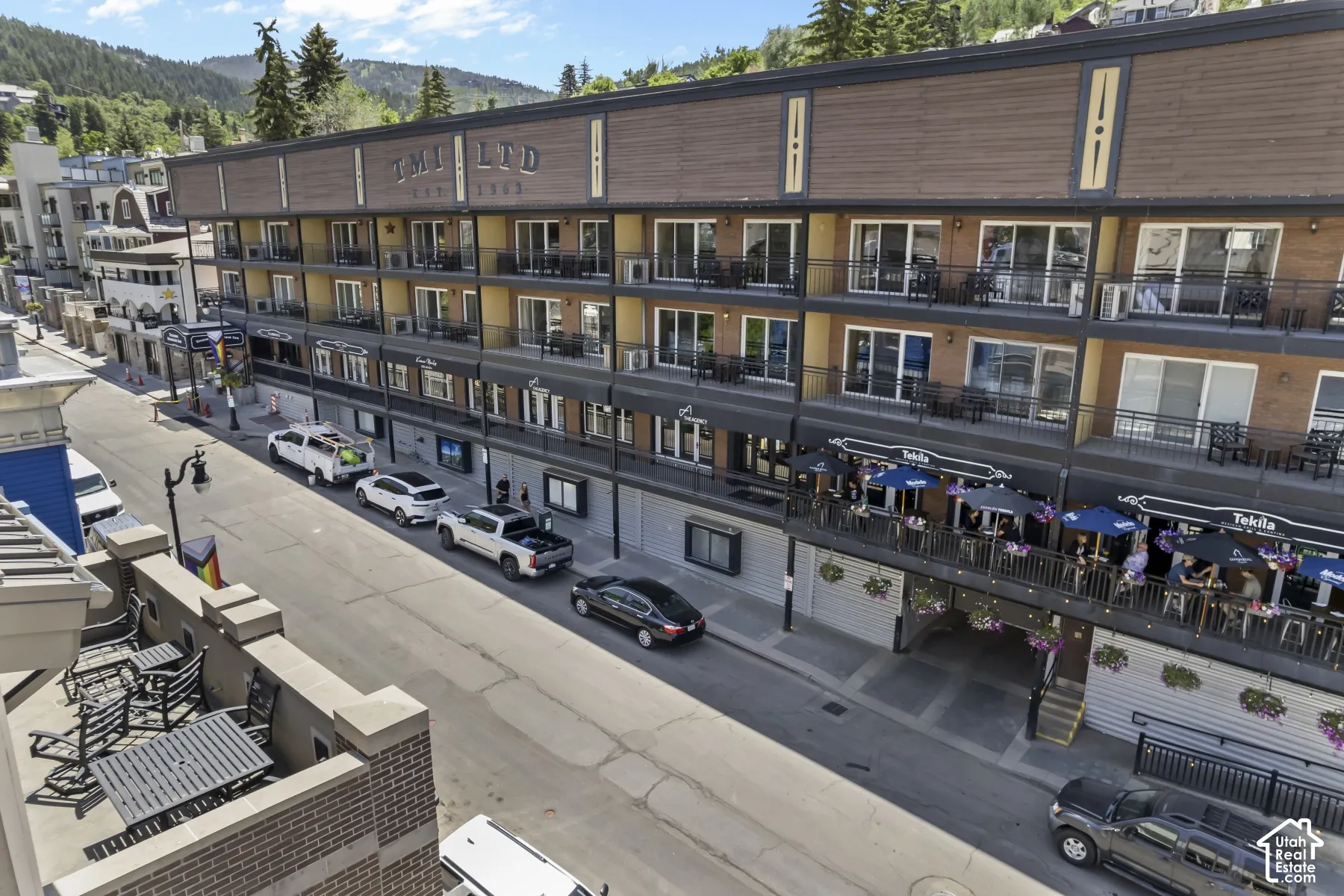 Multi-level building with individual balconies, ground-level retail spaces, and an upper residential facade featuring wood-look siding