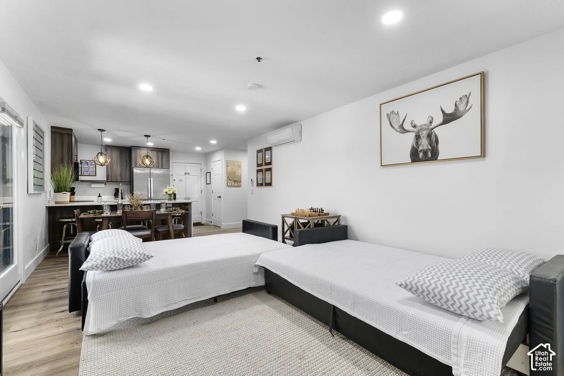 Open-concept living space featuring wood-finish flooring, recessed lighting, and a kitchen with dark-toned cabinetry, stainless steel appliances, and a central island with pendant lighting