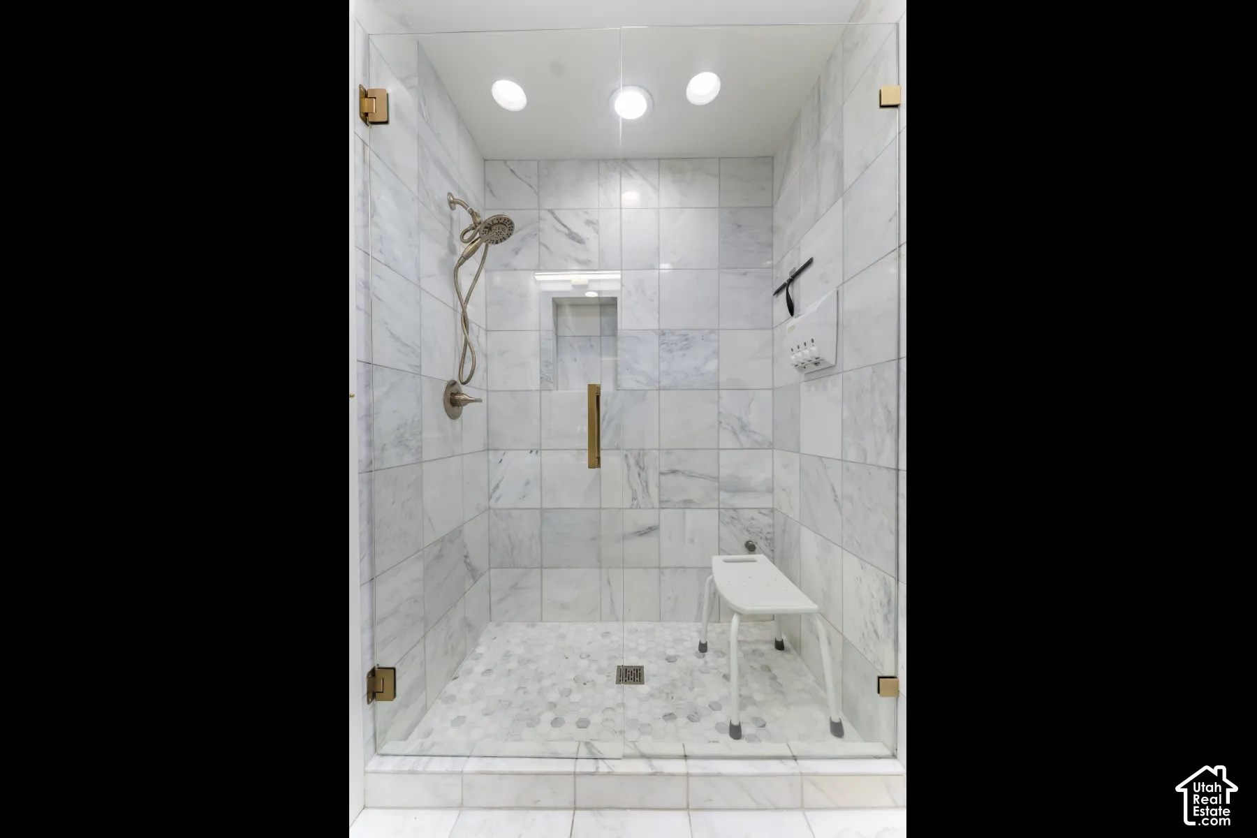 Glass-enclosed shower with white tiled walls and mosaic tile flooring