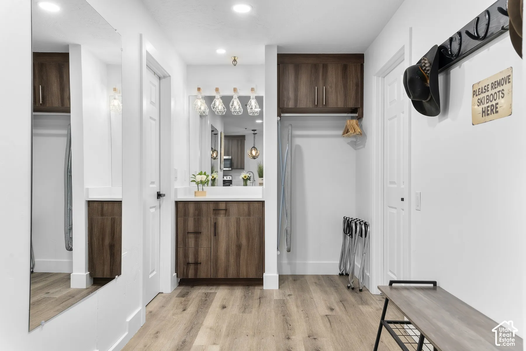 Wood-finish flooring, built-in vanity with white countertop, integrated sink, overhead lighting fixture, and a full-length mirror