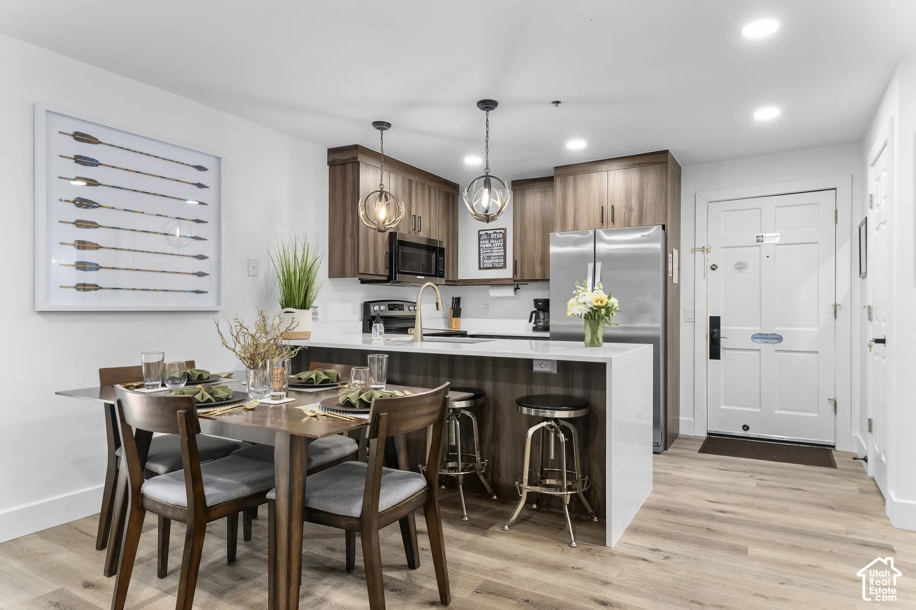 Wood-finish flooring throughout, kitchen with wood-finish cabinetry, stainless steel appliances, and a white countertop island with seating