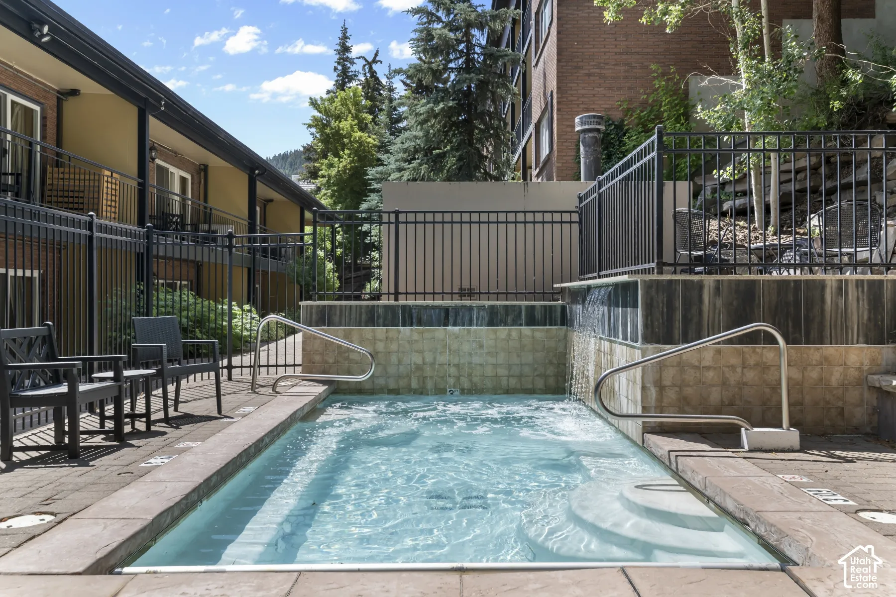 In-ground spa with integrated steps and handrails, complemented by a tiled surround and water feature