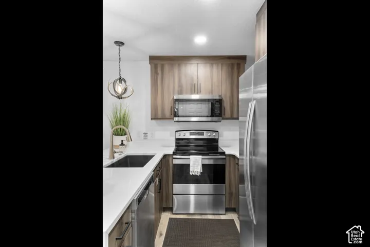 Kitchen featuring wood-finish cabinetry, stainless steel appliances, white countertops, and a single-basin sink