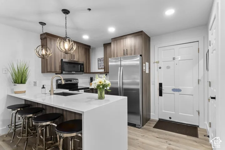 Kitchen featuring wood-finish cabinetry, stainless steel appliances, a white solid surface countertop, and wood-finish flooring