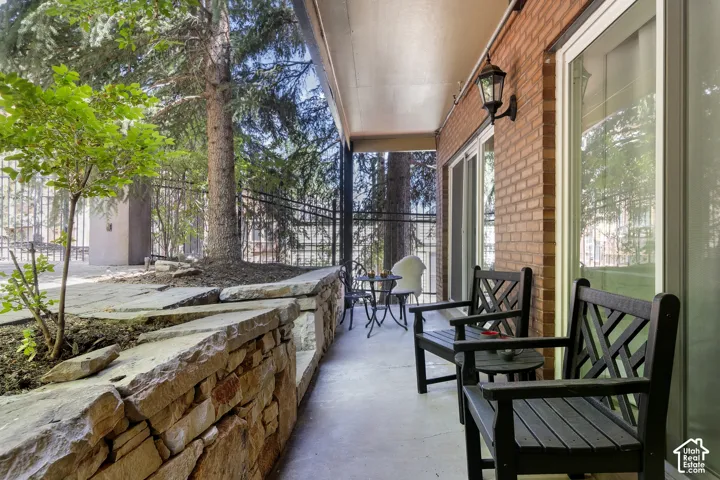 Covered patio featuring brick exterior, a stone retaining wall, and mature trees
