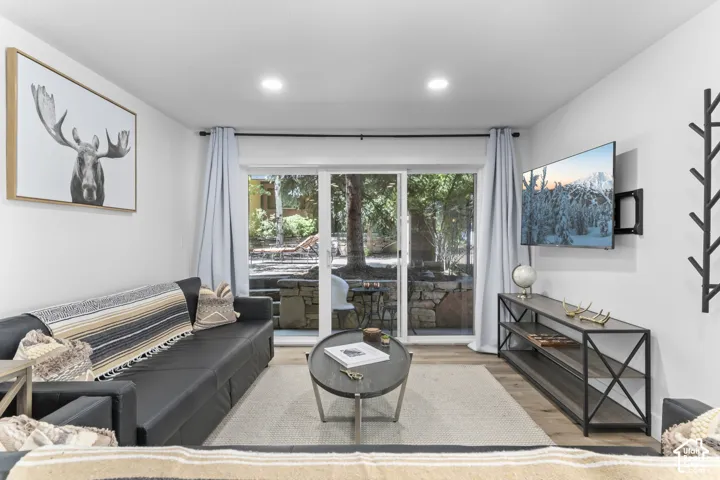 Recessed ceiling lighting, wood-finish flooring, sliding glass door to exterior, stone retaining wall, and wall-mounted television