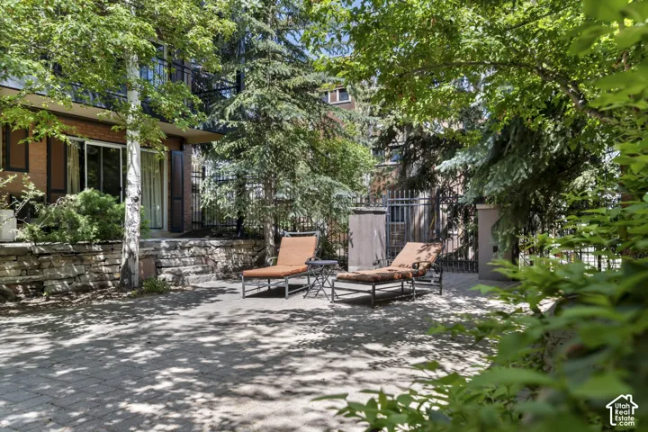 Paved patio area, stone retaining wall, sliding glass door, wrought iron fencing, mature trees