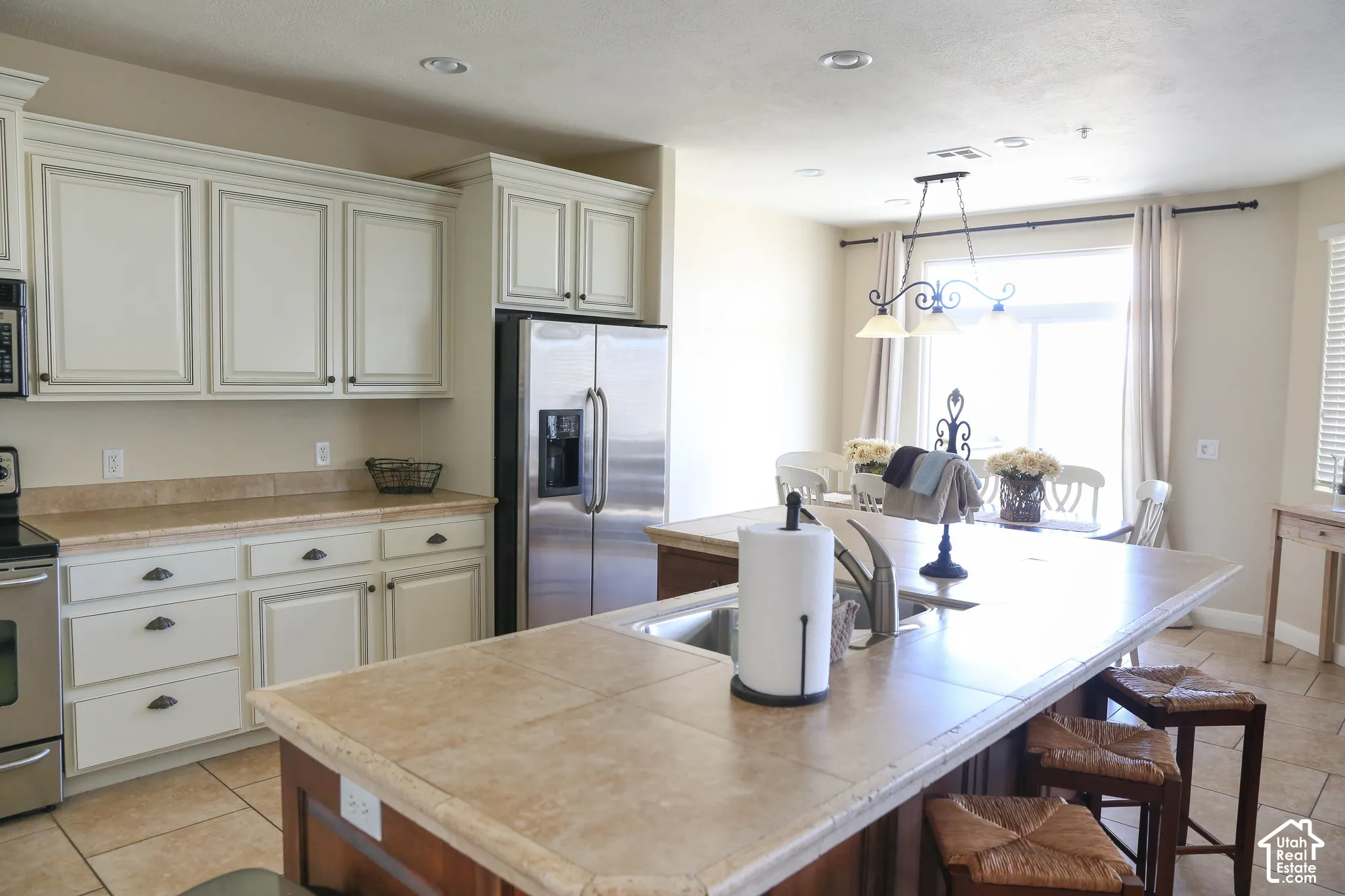 Kitchen featuring a large island with an integrated sink, paneled cabinetry, stainless steel appliances, and tile flooring