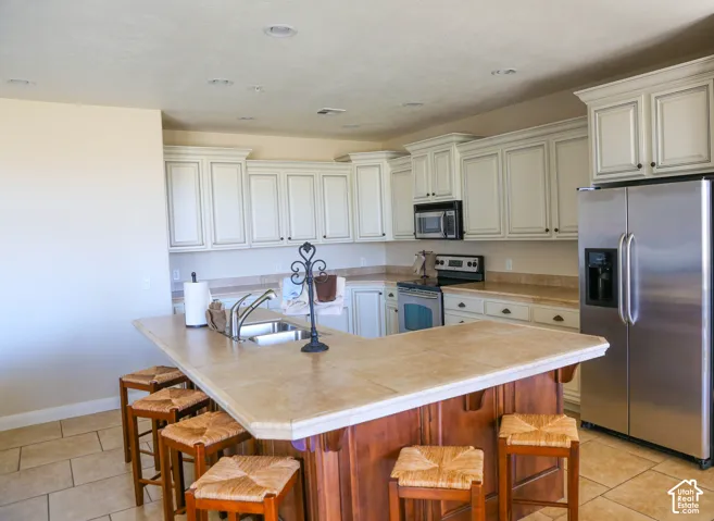 Kitchen featuring an island with a built-in sink, white cabinetry with dark hardware, stainless steel appliances, and tile flooring