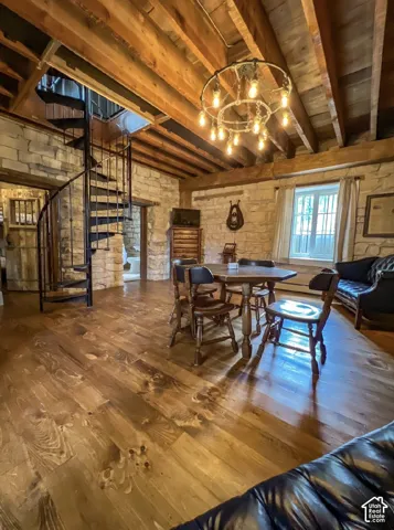 Exposed wood beam ceiling, stone accent walls, spiral staircase, wood-finish flooring, and a unique chandelier