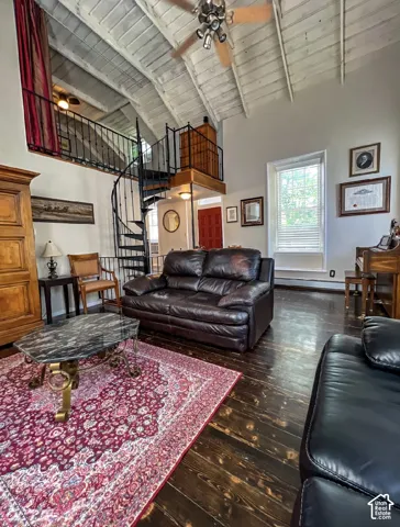 Exposed beam vaulted ceiling, spiral staircase with wrought iron railing, dark wood-finish flooring, and a red paneled entry door