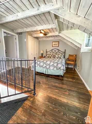 Angled wood-plank ceiling with exposed beams, wood-finish flooring, and a built-in ceiling fan