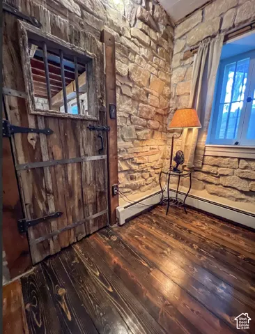 Exposed stone wall, wood-finish flooring, wood plank door with iron hardware, and a window with light-colored drapes
