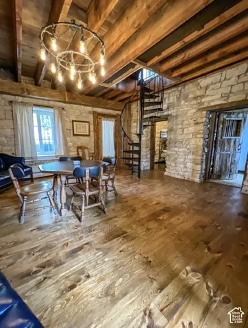 Exposed wood beam ceiling, stone accent walls, industrial-style spiral staircase, wood-finish flooring, and a wagon wheel chandelier