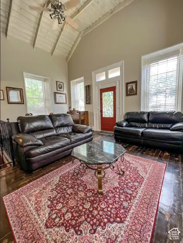 Vaulted ceiling with exposed wood beams, wood-finish flooring, red entry door with decorative glass, and multiple windows