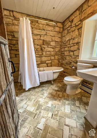 Stone-clad walls, clawfoot tub, pedestal sink, wood-finish plank ceiling, and herringbone pattern floor tiling