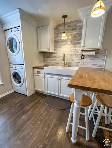 Wood-finish flooring with white cabinetry, a farmhouse sink, and a stacked washer and dryer