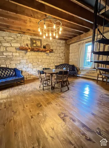 Stone accent wall, exposed wood beam ceiling, wood-finish flooring, and a spiral staircase