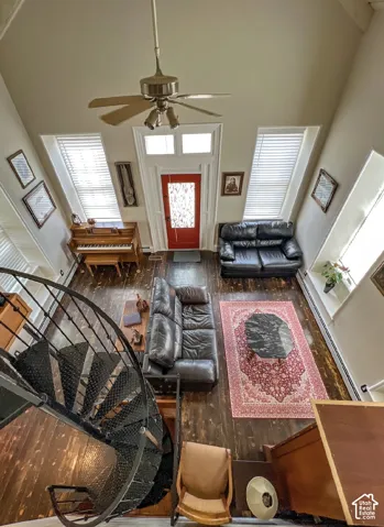 Spiral staircase, wood-finish flooring, ceiling fan, red entry door with decorative glass, vaulted ceiling