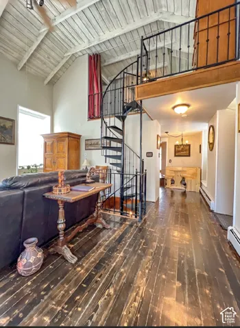 Vaulted wood-paneled ceilings, dark wood-finish flooring, and a black wrought iron spiral staircase define this living area
