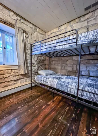Stone accent wall with wood-finish flooring and a white window frame