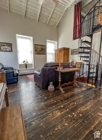 Vaulted ceiling with exposed wood beams, dark wood-finish flooring, and a black wrought iron spiral staircase