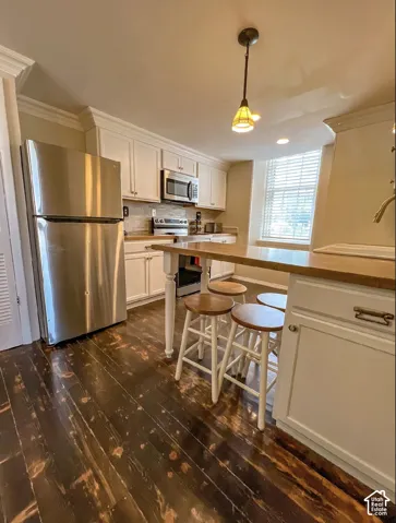 Kitchen featuring wood-finish flooring, white cabinetry, stainless steel appliances, and a tiled backsplash