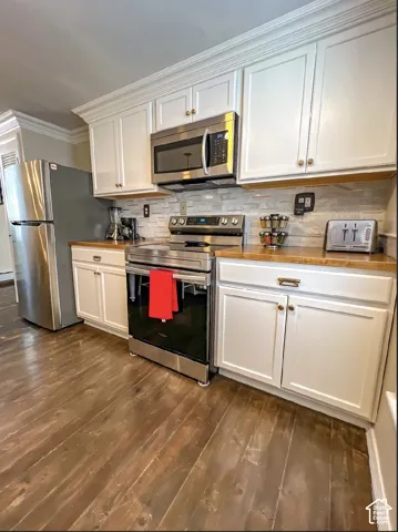 White cabinetry with crown molding, stainless steel appliances, wood-finish flooring, and a tiled backsplash