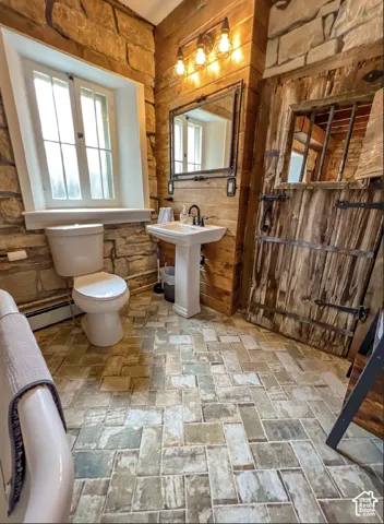 Stone accent walls, wood plank details, pedestal sink with black fixtures, rustic wood door, and mosaic tile flooring