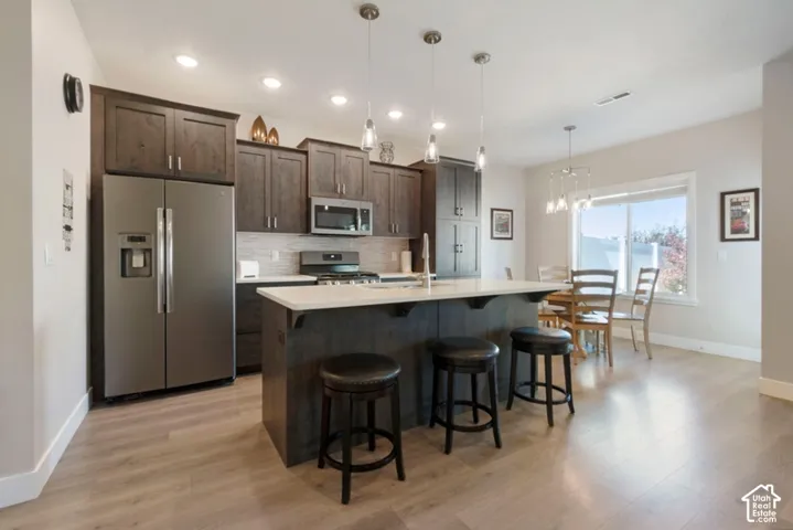 Kitchen featuring dark wood-finish cabinetry, stainless steel appliances, a center island with countertop seating, and light wood-finish flooring