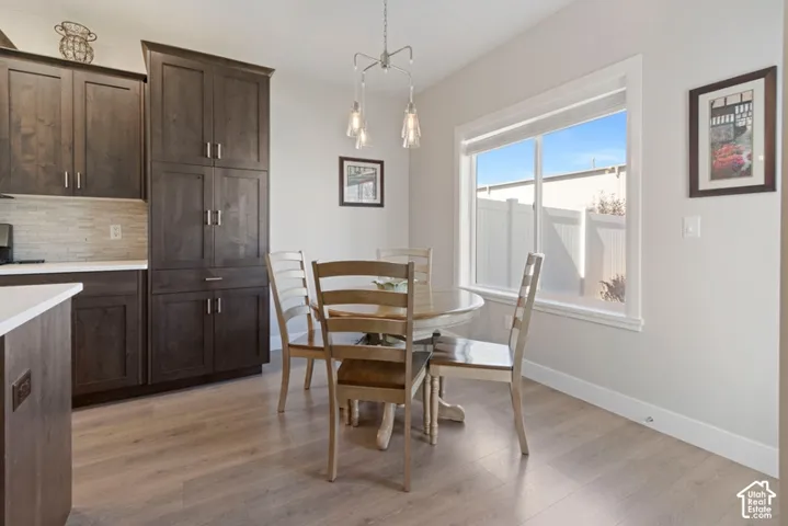 Built-in dark wood-finish cabinetry, light wood-finish flooring, white countertops, tiled backsplash, and a contemporary pendant light fixture