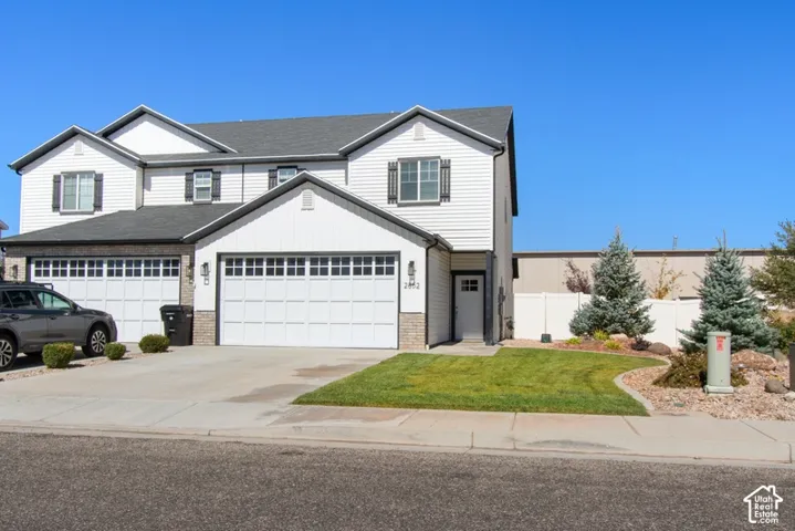 White siding exterior with dark trim accents, attached two-car garage, manicured lawn, and decorative landscaping