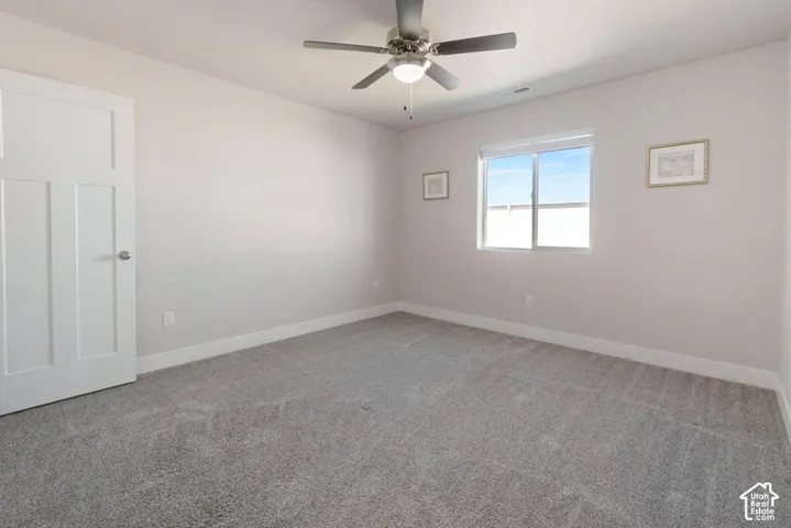 Gray wall-to-wall carpeting, white interior door, ceiling fan with integrated lighting, and a single window with white trim