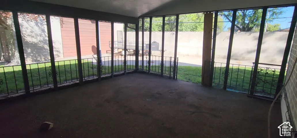 Screened-in porch featuring a concrete floor, dark metal railing, and wood support beams