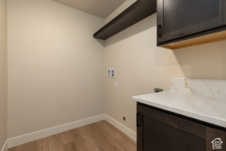 Wood-finish flooring, white baseboards, dark wood-finish cabinetry, white countertop with veining, and a dark wood-finish floating shelf