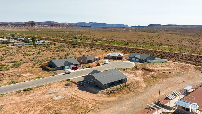 Residential street with multiple single-story homes, unlandscaped lots, and distant mesa formations