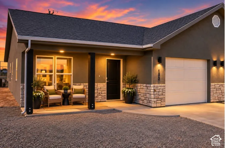 Modern stucco exterior with stone veneer accents, covered entry porch, attached garage, and multiple exterior wall sconces