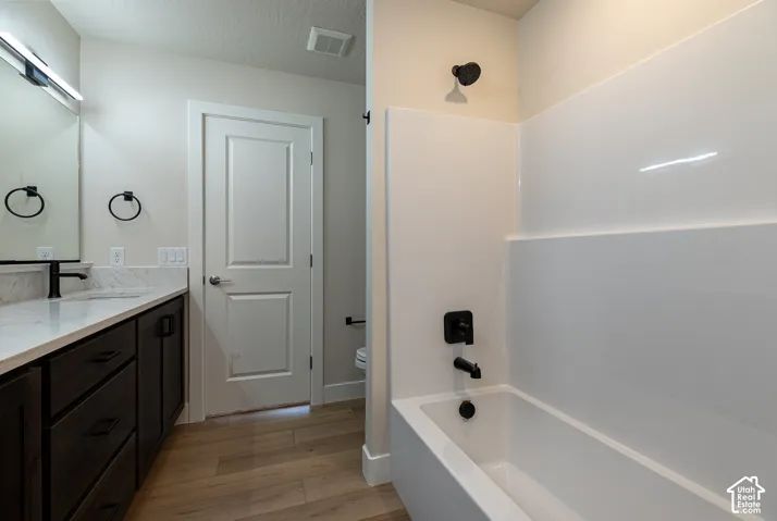 Wood-finish flooring, dark wood-tone vanity with white countertop, integrated sink, and black fixtures
