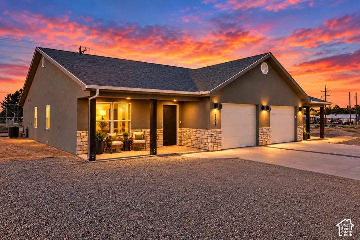 Stucco exterior with stone accent detailing, covered front porch, two-car garage with overhead lighting, and concrete driveway