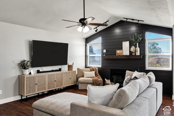 Vaulted ceiling with a ceiling fan, black shiplap accent wall, two large windows, wood-finish flooring, and a built-in fireplace