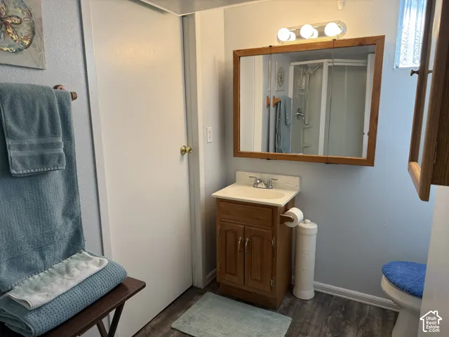 Wood-finish flooring, single vanity with wood cabinetry, and a mirrored medicine cabinet