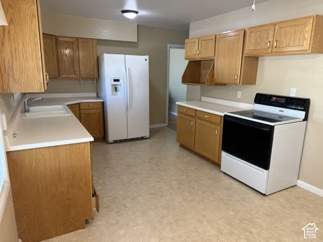Spacious kitchen with wood-finish cabinetry, solid surface countertops, a dual basin sink, and a white side-by-side refrigerator