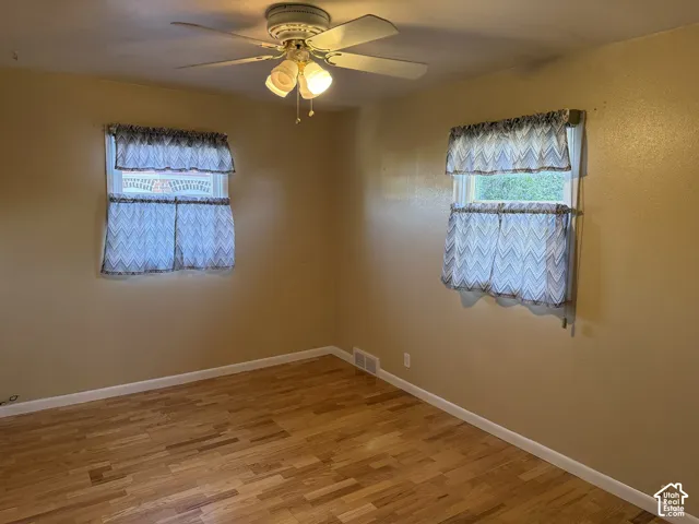 Wood-finish flooring, two windows, and a ceiling fan with integrated lighting