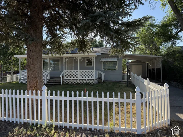 Exterior featuring a white picket fence, covered front porch with lattice detailing, and a carport