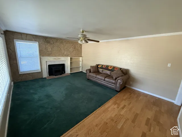 Stone accent wall with a fireplace, built-in shelving, ceiling fan, and mixed flooring with carpet and wood-finish