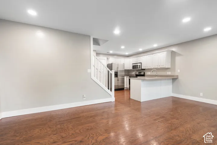 Wood-finish flooring, recessed lighting, white kitchen cabinetry, stainless steel appliances, and a built-in kitchen island with counter seating