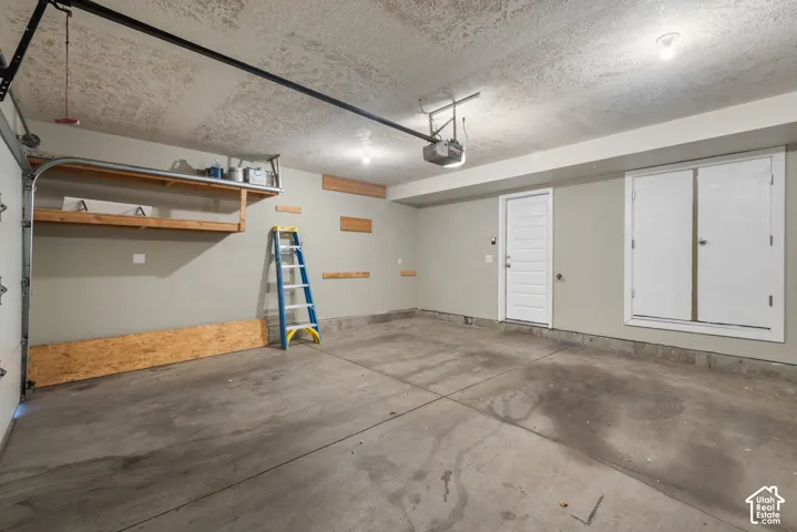 Garage featuring a concrete floor, built-in shelving, an overhead door opener, a side door, and built-in storage cabinets