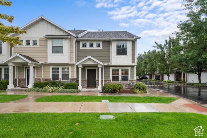 Multi-story townhouse with stone-accented facade, covered entry, and landscaped front yard