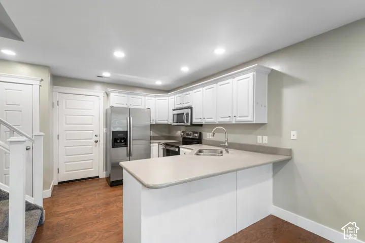 Kitchen featuring white cabinetry, stainless steel appliances, a bar-height counter, a single-basin sink, and wood-finish flooring