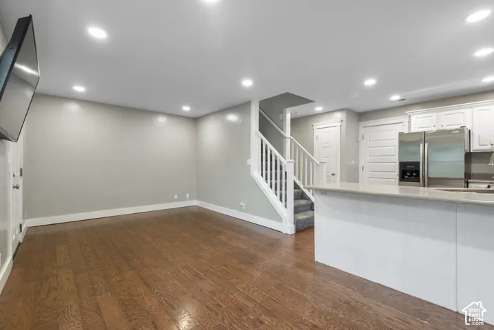 Wood-finish flooring, recessed lighting, white kitchen cabinetry, stainless steel refrigerator, and a built-in kitchen island with stone countertop